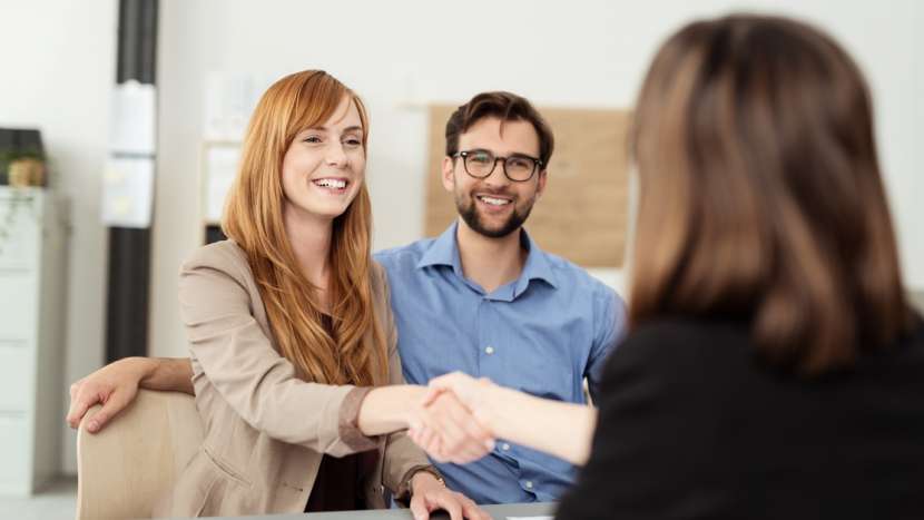 female banker shaking hands with customers sitting at a desk