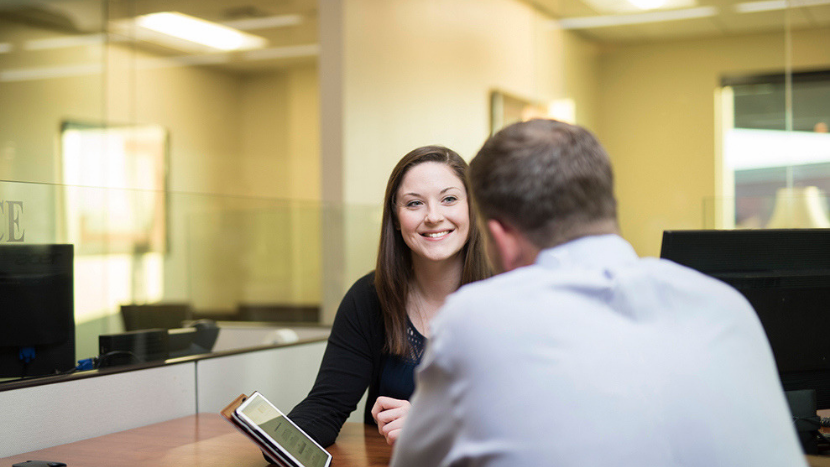 banker at desk smiling at customer with tablet