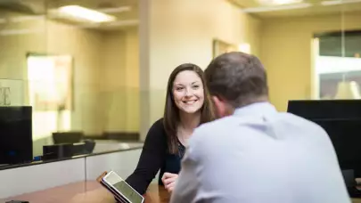 banker at desk smiling at customer with tablet