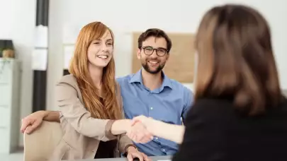 female banker shaking hands with customers sitting at a desk