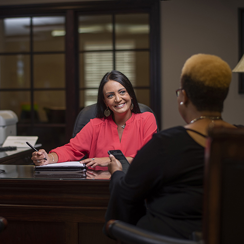 Woman sitting at desk talking to another woman.